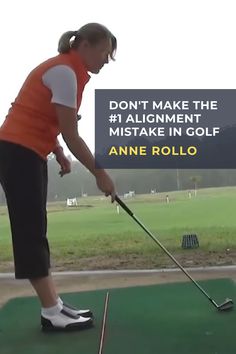 a woman in an orange vest hitting a golf ball with a club on the green