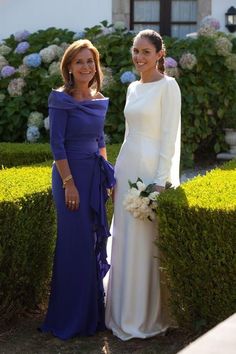 two women standing next to each other near bushes