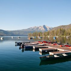 several canoes are docked at the end of a pier on a lake with mountains in the background