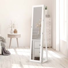 a white floor standing mirror next to a table with flowers on it in a room