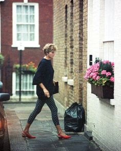 the woman is walking down the street with her hand in her pocket and wearing red shoes