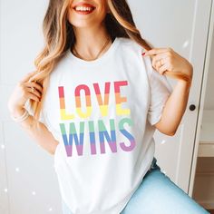 The "Love Wins" Graphic Tee is more than just a garment; it's a bold declaration of support for the LGBTQ+ community and a celebration of love in all its forms. Crafted with care and attention to detail, this tee is designed for both comfort and style, making it the perfect choice for expressing your pride and solidarity. The powerful "Love Wins" graphic boldly proclaims the triumph of love over hate, serving as a beacon of hope and acceptance. Whether you're marching in a pride parade, attendin White Pre-shrunk Top For Pride, Pre-shrunk Crew Neck T-shirt For Pride, Relaxed Fit Crew Neck T-shirt For Pride, Pride Festival Crew Neck Top, Pride Screen Print Crew Neck T-shirt, Pride Funny Print Crew Neck T-shirt, Pride Graphic Print Crew Neck Top, White Text Print Tops For Pride, Pride Letter Print Crew Neck T-shirt