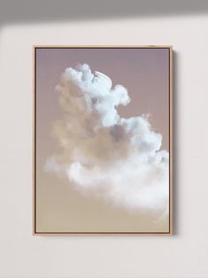 a framed photograph of a cloud in the sky with a light brown frame hanging on a wall