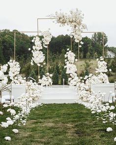 an outdoor ceremony setup with white flowers and gold framed chairs on the grass in front of it