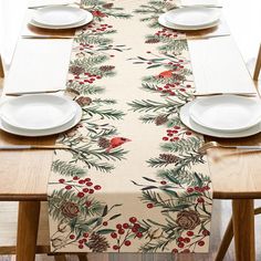 the table is set with white plates and placemats, which are decorated with evergreen leaves