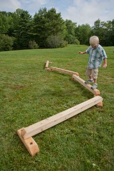 a little boy standing on top of a wooden sees - o - log in the grass