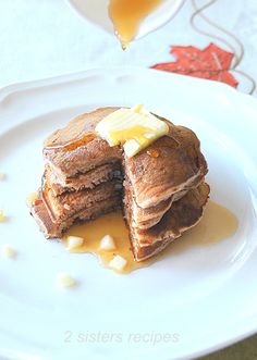 a stack of pancakes with syrup and butter on a white plate next to a glass of orange juice