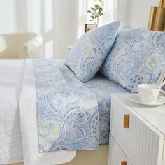 a bed with blue and white bedspread next to a dresser in a bedroom