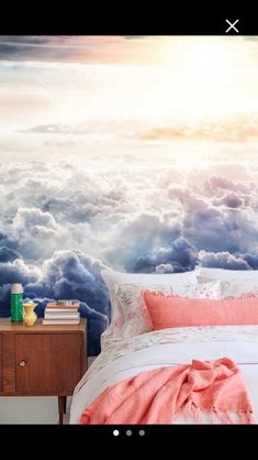 there is a bed in front of a wall with clouds on it and the sun shining through