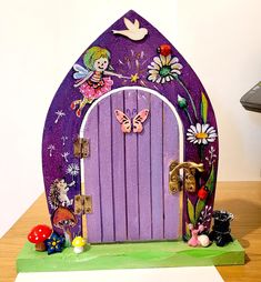 a purple fairy door with flowers and butterflies on the front is surrounded by little figurines