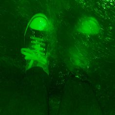 someone's feet in the water with green light on them and their shoes lit up