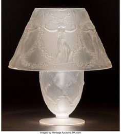 a glass lamp with a white shade on it's base and an angel design