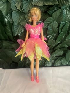 a barbie doll wearing a pink and yellow tutu skirt, with green leaves in the background