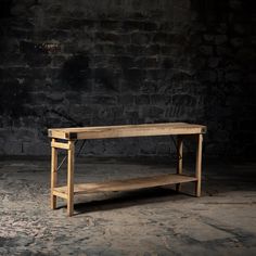 a wooden table sitting on top of a stone floor next to a brick wall with no one around it