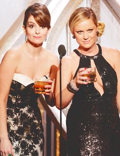 two women standing next to each other in front of a microphone and holding drinks together