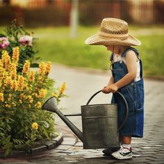 a little boy with a straw hat and overalls is holding a metal watering can