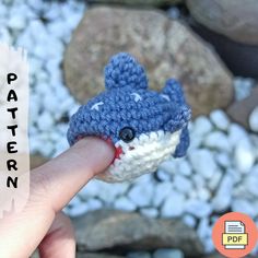 a hand holding a tiny crocheted blue and white toy shark in it's mouth