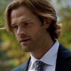 a close up of a person wearing a suit and tie with trees in the background