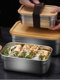 two stainless steel containers with food in them on a wooden table next to another container