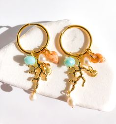 CORAL DREAMLAND Step into a world of enchantment with our "Coral Dreamland" hoop charm earrings. Imagine the gentle sway of turquoise waters captured in a light blue crystal bead, evoking the essence of tropical paradise. The 18k gold-plated coral charm adds a touch of elegance and sophistication, while the natural freshwater pearls and adorable seashell infuse a playful charm. Embrace the whimsical beauty of these earrings, reminiscent of a dreamy coral reef under the sun-kissed sea. Let your s Ocean-inspired Jewelry With Dangling Charms For Gifts, Beach Jewelry With Dangling Charms, Ocean-inspired Gold Jewelry With Dangling Charms, Gold Ocean-inspired Jewelry With Dangling Charms, Ocean-inspired Dangle Charms Jewelry, Metal Hoop Earrings With Pearl Charm For Gift, Metal Hoop Earrings With Pearl Charm As A Gift, Beach Jewelry With Dangling Metal Charms, Coral Jewelry For Summer Gifts