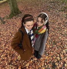 two young women standing in the leaves with headphones on their ears, looking at each other