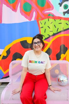 a woman sitting on top of a pink bench in front of a colorful wall and painting