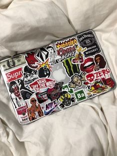 an apple laptop covered in stickers on a bed