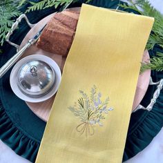 a yellow table runner on a plate with a silver teapot and pine tree decoration