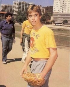 a young man holding a catchers mitt while standing next to another person on a sidewalk