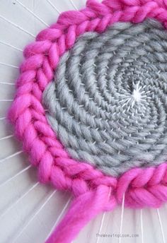 a pink and gray crochet doily with yarn in the center on a white surface