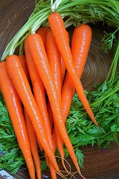 some carrots are laying on top of the green leafy vegetables in a bowl