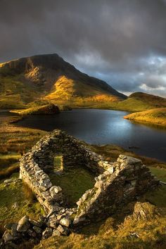 an old stone building sitting on top of a lush green hillside next to a lake