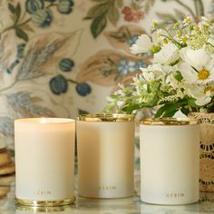 three white candles sitting on top of a counter next to a vase filled with flowers