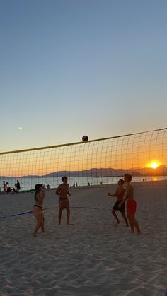 people playing volleyball on the beach at sunset