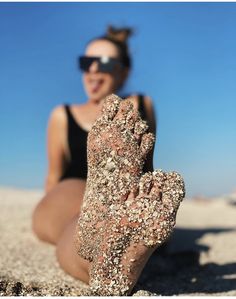 a woman sitting in the sand with her feet up