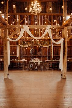 the inside of a barn decorated with white draping and chandelier hanging from the ceiling