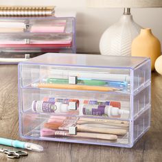 two clear drawers with pens, markers and pencils in them on a wooden table