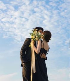 a man and woman standing next to each other under a blue sky with white clouds