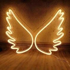 a neon angel sign sitting on top of a wooden floor next to a light bulb