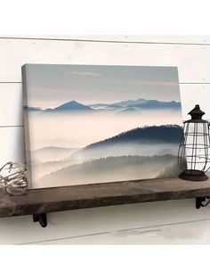 a painting hanging on the wall above a shelf with a lamp and lantern in front of it