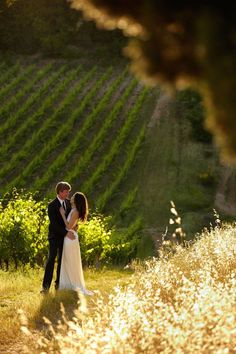 a bride and groom standing in the middle of a field with rows of vines behind them