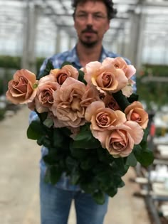 a man holding a bouquet of pink roses in a greenhouse