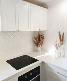 a kitchen with white cabinets and a black stove top in the center, next to a vase filled with dry grass