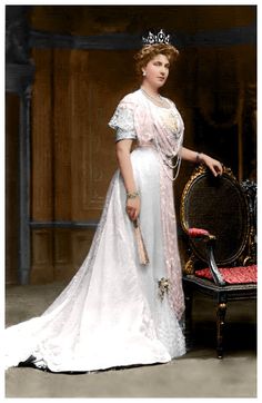 an old photo of a woman wearing a tiara standing next to a chair and looking at the camera