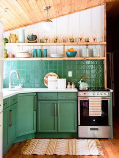 a kitchen with green cabinets and white counter tops is pictured in this image, there are dishes on the shelves above the stove