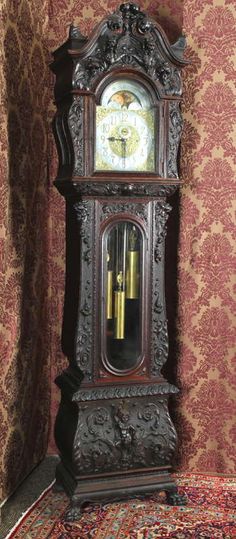 an ornate grandfather clock with pendulums on the front and sides, against a red wallpapered background