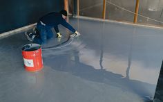 a man is painting the floor in an empty room with a bucket and paint roller