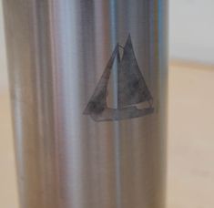 a stainless steel cup with a sailboat sticker on the side, sitting on a table