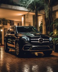 a black mercedes suv parked in front of a building at night with its lights on