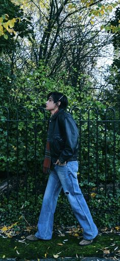 a man walking in front of a black fence with leaves on the ground and trees behind him